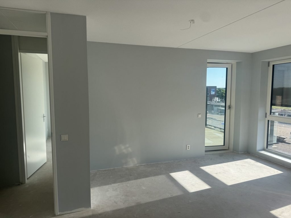 Woonkamer van een nieuw appartement met balkondeur en egaal lichtgrijs gesausde wanden