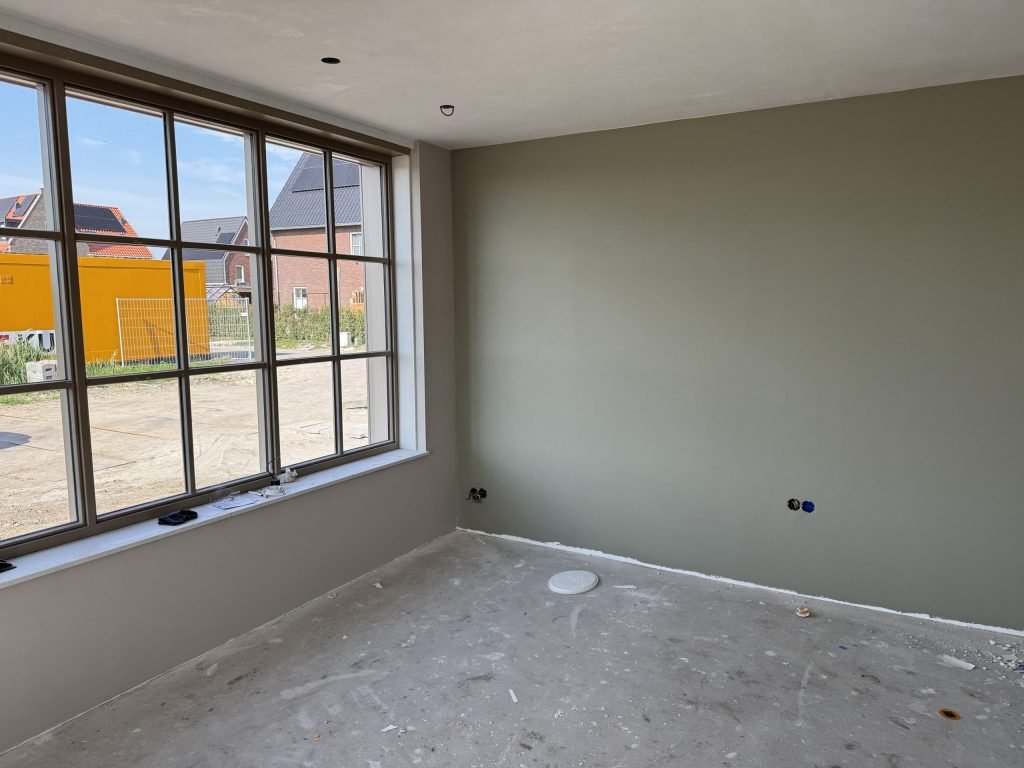 Kamer in een nieuwbouwhuis met een grijsgroen gesausde wand naast een groot roedenraam