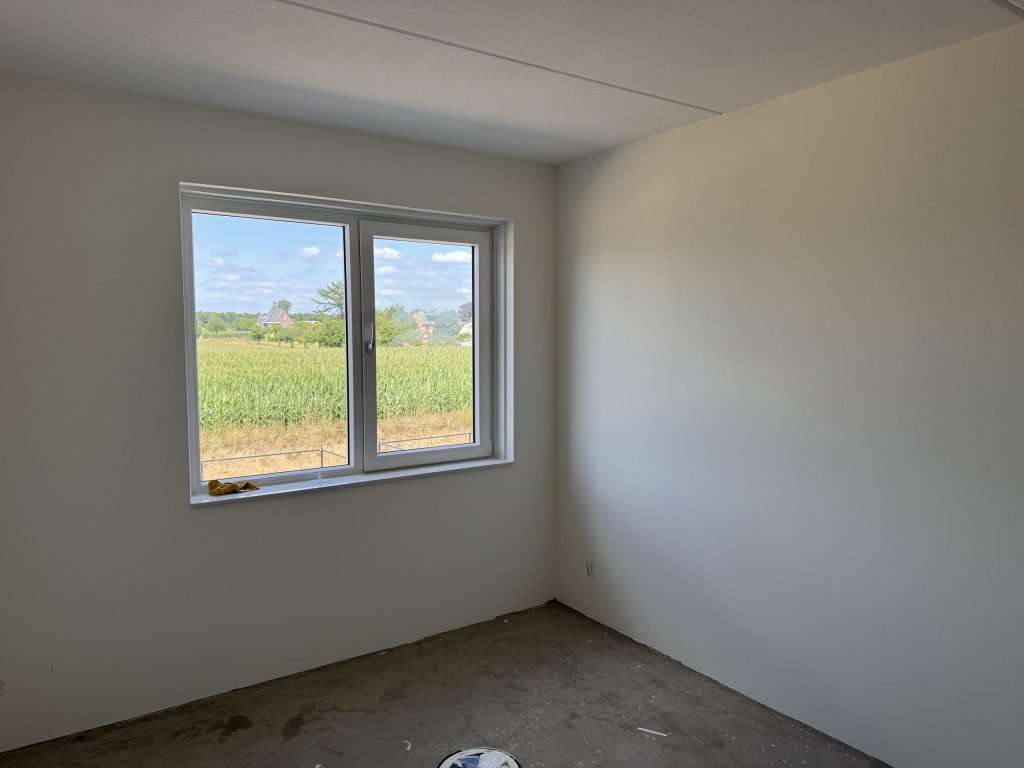 Lege slaapkamer in een nieuwbouwwoning met glad afgewerkte witte wanden en uitzicht op het land
