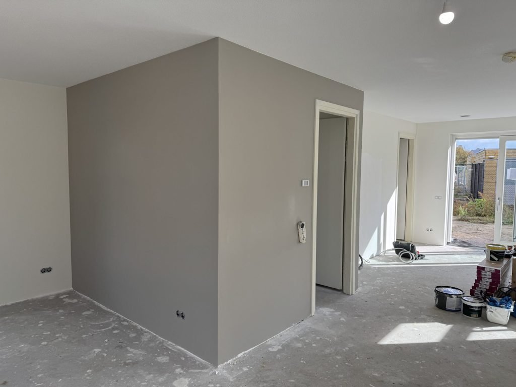 Gesausde grijze wand rond de meterkast in een nieuwbouwwoning, met verfemmers op de betonvloer
