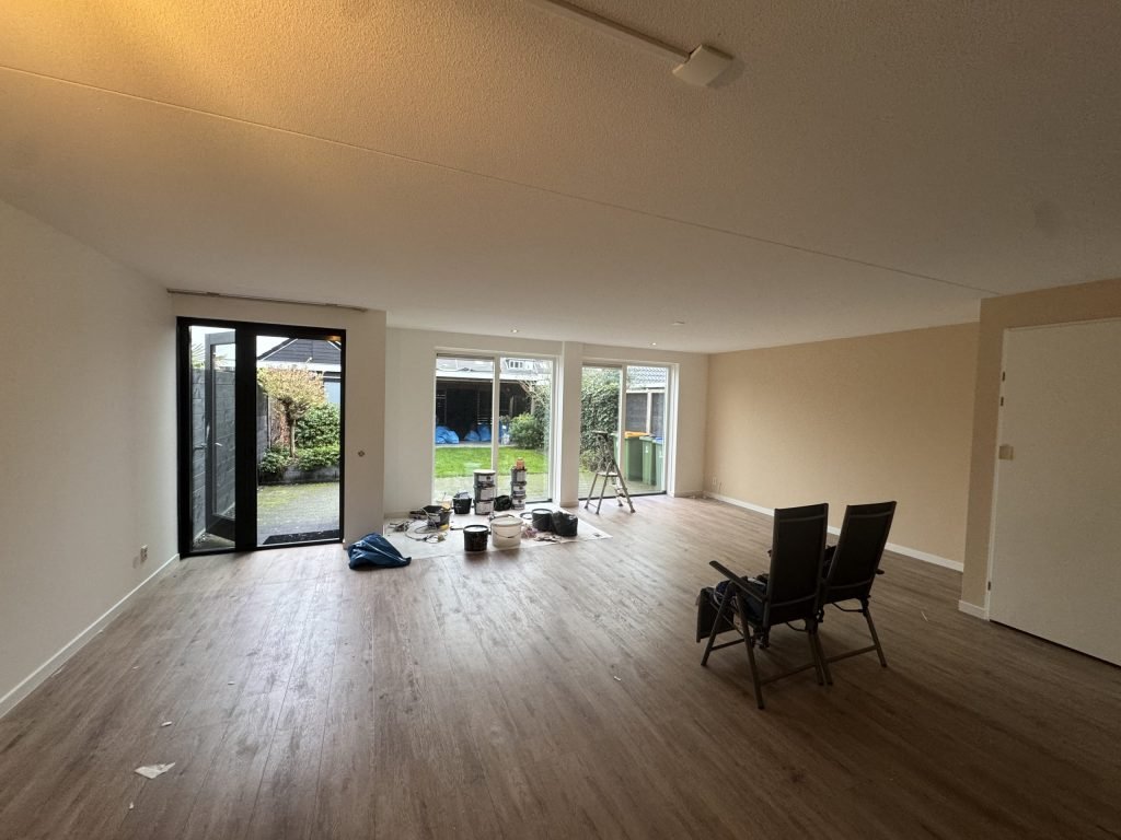 Ruime woonkamer met lichte wanden, laminaat en tuindeuren tijdens het afwerken